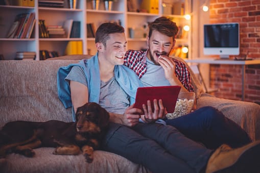 Two men eating popcorn on couch with dog